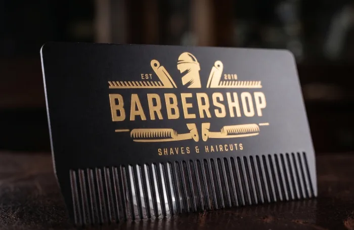 Black metal business card die cut into a comb shape with gold foil barbershop branding.