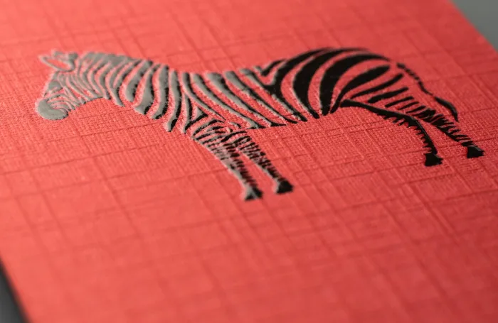 Red linen business card featuring a tactile black zebra illustration with raised glossy stripes.