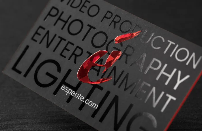 Black suede business card for an entertainment and production company featuring glossy black text, white lettering, and a faceted red foil emblem.