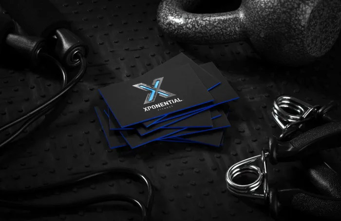 Black silk fitness cards for Xponential Fitness feature metallic foil logos, white lettering, and vivid blue painted edges amid gym equipment.
