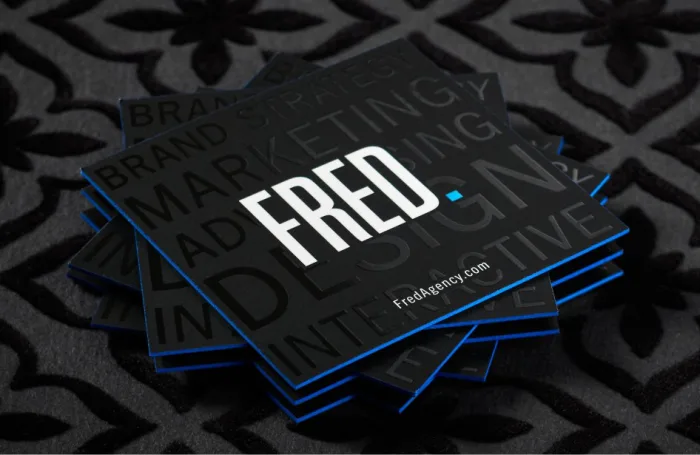 Square black suede marketing agency business cards for Fred featuring glossy spot UV typography and electric blue edges.