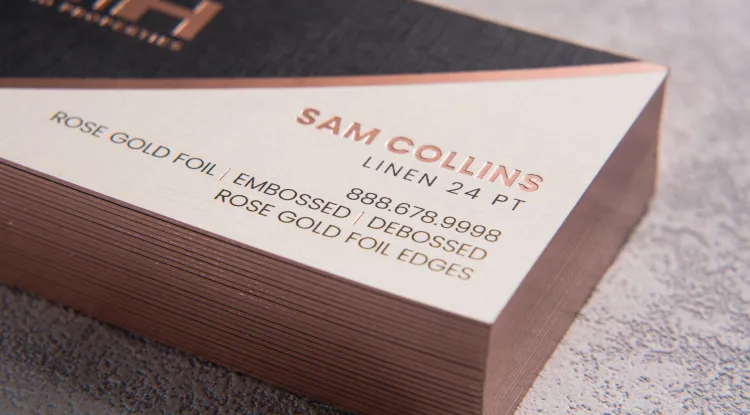 Cream linen business cards for Sam Collins featuring raised rose gold foil lettering and matching metallic foil edges.