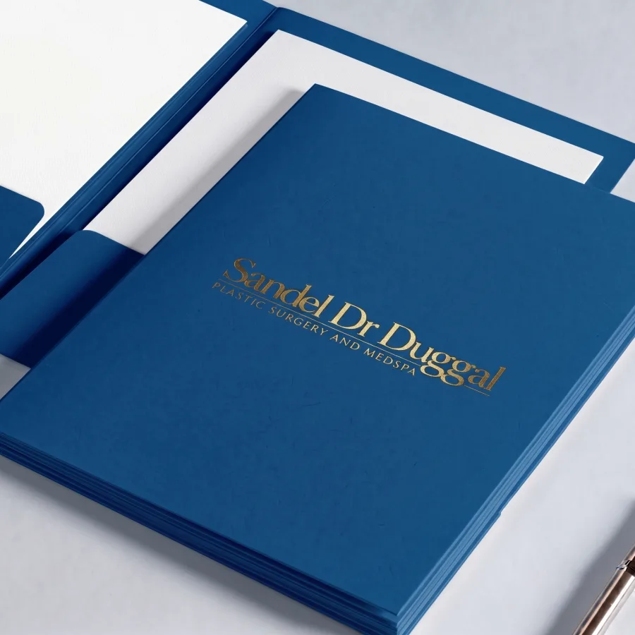Sandel Dr Duggal plastic surgery and medspa presentation folders in rich blue display gleaming gold foil lettering and matching interior pockets.
