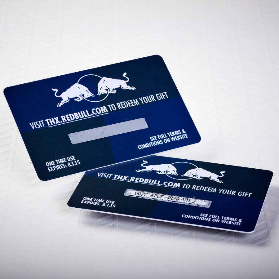Two blue and white plastic Red Bull gift cards display the bull logo, website URL, and a silver scratch-off panel with graphic appeal.