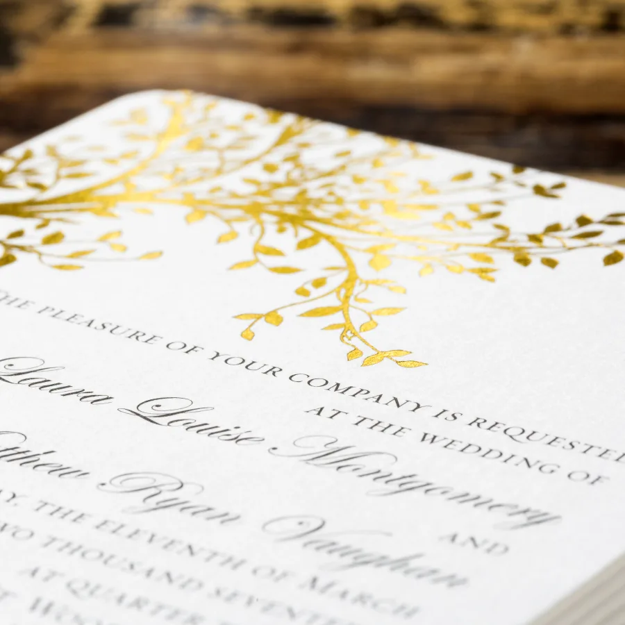 A white wedding invitation postcard features gleaming gold foil branches and dark text in a tactile finish.