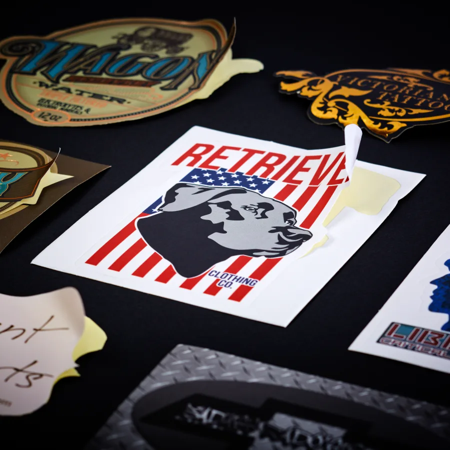 Several assorted die-cut stickers featuring a red, white, and blue Retrieve Clothing Co. dog design with peeling backing in a graphic finish.