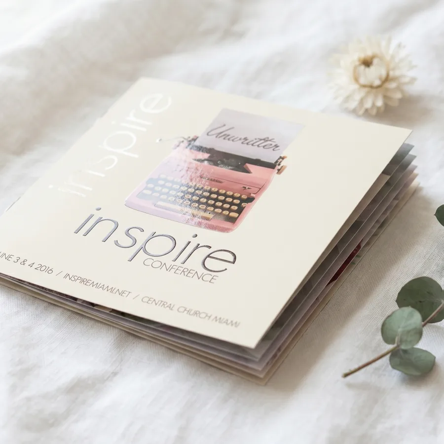 A multi-page square catalog for Inspire Conference features a pink typewriter photo, debossed silver lettering.